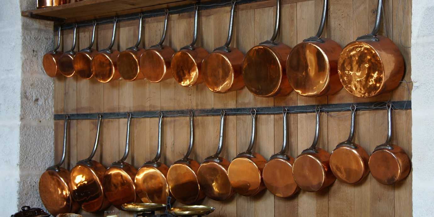 21 copper pots and pans hanging on a wall.