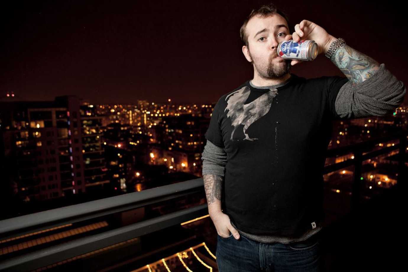 Jason Lengstorf on a balcony at night drinking beer.